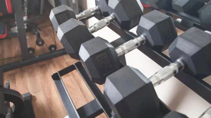 A close-up of a rack holding several hexagonal black dumbbells in a gym setting.