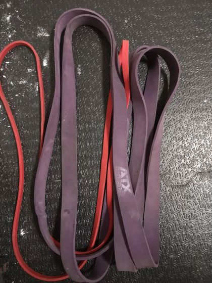 Two resistance bands: one red and one purple, lying on a textured black surface.