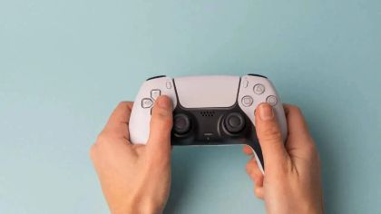 A pair of hands holding a PlayStation 5 controller against a light blue background.