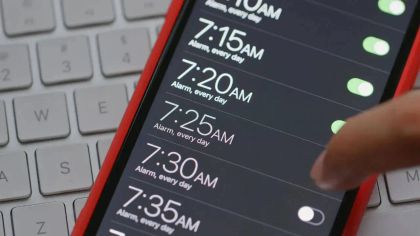 Close-up of a phone screen showing multiple alarm times set for 7:10 AM to 7:35 AM, beside a computer keyboard.