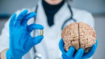 A medical professional in gloves holds a brain model in one hand and a capsule in the other, symbolizing medicine.