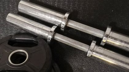 Two metal barbells with textured grips on a dark rubber mat, next to a black weight plate.