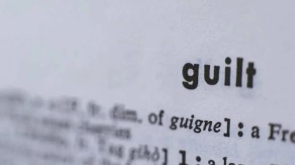 Close-up of a printed page showing the word "guilt" in bold, with blurred text in the background.