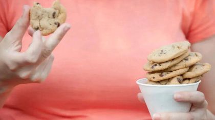 A person holding a cookie in one hand and a cup stacked with cookies in the other, wearing a pink shirt.