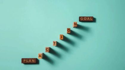 Wooden blocks spelling "PLAN," "ACTION," and "GOAL" arranged in a diagonal line on a light blue background.