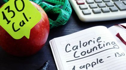 A red apple with a note showing "130 Cal," next to a notebook labeled "Calorie Counting" and a calculator.