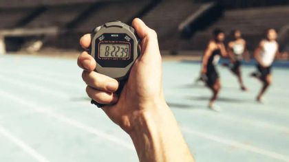 A hand holding a stopwatch displaying the time 8:22:39, with runners in the background on a track.