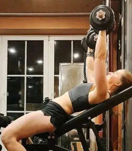 A person in a gym performing a dumbbell bench press on a workout bench.