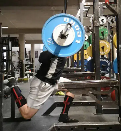 A person performs a weighted squat in a gym, focusing on strength training with a barbell on their back.