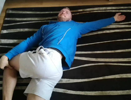 A person in a blue jacket lies on a striped rug, arms outstretched and legs in a bent position.